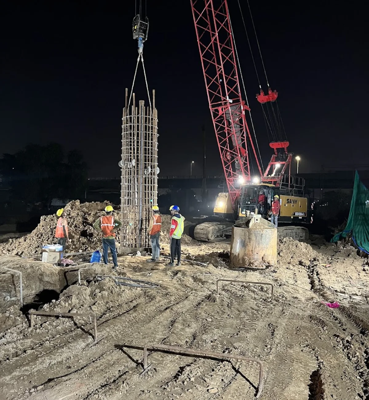 Crane lifting a pile cage during night foundation work